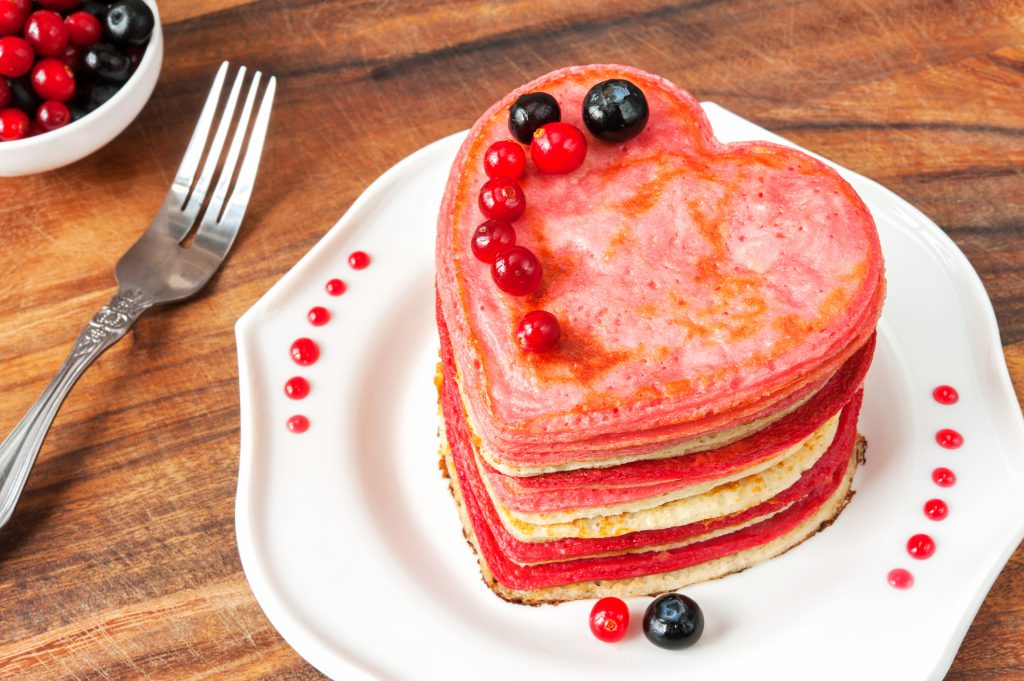 Festive dish-Valentines day homemade pink colored heart shaped pancakes with berries. Vibrant indoors horizontal closeup image.